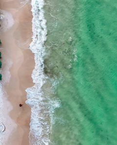 Tide breaking on Destin Beach. Emerald green waters in the morning as waves crash on Destin Beach. Fish swimming in low tide. Beach chairs and umbrellas set up in the morning for tourists and vacationers to relax on a Florida day.