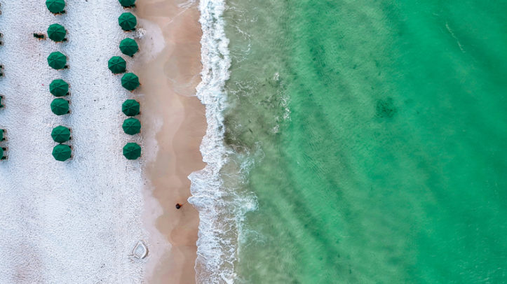 Tide breaking on Destin Beach. Emerald green waters in the morning as waves crash on Destin Beach. Fish swimming in low tide. Beach chairs and umbrellas set up in the morning for tourists and vacationers to relax on a Florida day.